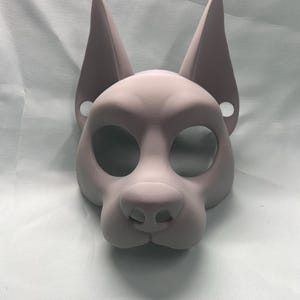 May include: A light purple dog mask with large, pointed ears and eye holes. The mask has a rounded snout and is made of a smooth material. The mask is designed to be worn on the face.