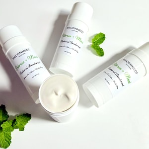 May include: Three white cylindrical containers of Reconnect Skincare Citrus + Mint Natural Deodorant, each labeled Net Wt 3 oz. One container is open, revealing a smooth, off-white cream, accompanied by two fresh green mint leaves.