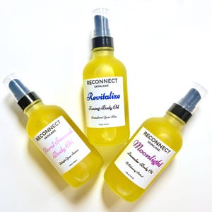 May include: Three clear glass bottles filled with bright yellow body oil, each topped with a black pump dispenser. The labels read Reconnect Skincare with the names Revitalize Toning Body Oil, Floral Sensual Body Oil, and Moonlight Lavender Body Oil.