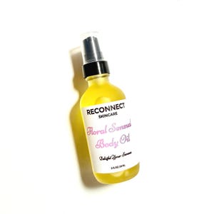 May include: A clear glass bottle filled with yellow body oil, featuring a black pump dispenser. The white label reads RECONNECT SKINCARE, Floral Sensual Body Oil, Delight Your Senses, and 2 FL OZ / 59 ML in black and pink text.