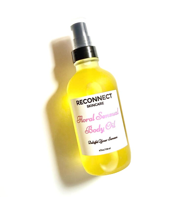 May include: A clear glass bottle filled with bright yellow body oil, featuring a black pump dispenser. The white label reads RECONNECT SKINCARE, Floral Sensual Body Oil, Delight Your Senses, and 4 fl oz/118 ml in black and pink text.
