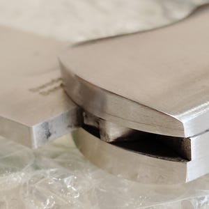 May include: Close-up of a stainless steel cleaver knife. The blade is rectangular and the handle is curved. The knife appears to be new and unused. The image is well-lit, highlighting the metallic sheen of the steel.