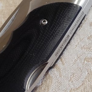 May include: A close-up shot of a folding knife featuring a black, textured handle and a silver blade. The blade is inscribed with "BROWNING MORGAN, UTAH". The knife is partially open, displaying its sharp edge.