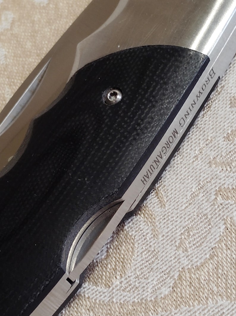 May include: A close-up shot of a folding knife featuring a black, textured handle and a silver blade. The blade is inscribed with "BROWNING MORGAN, UTAH". The knife is partially open, displaying its sharp edge.