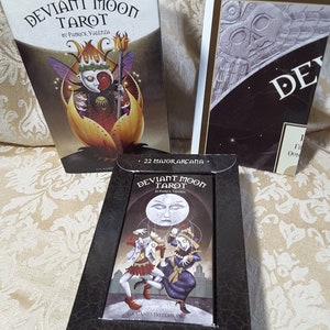 May include: A tarot card deck set, featuring the "Deviant Moon Tarot" by Patrick Valenza. The boxes display illustrations of whimsical figures and the deck includes 22 Major Arcana and 56 Minor Arcana cards.