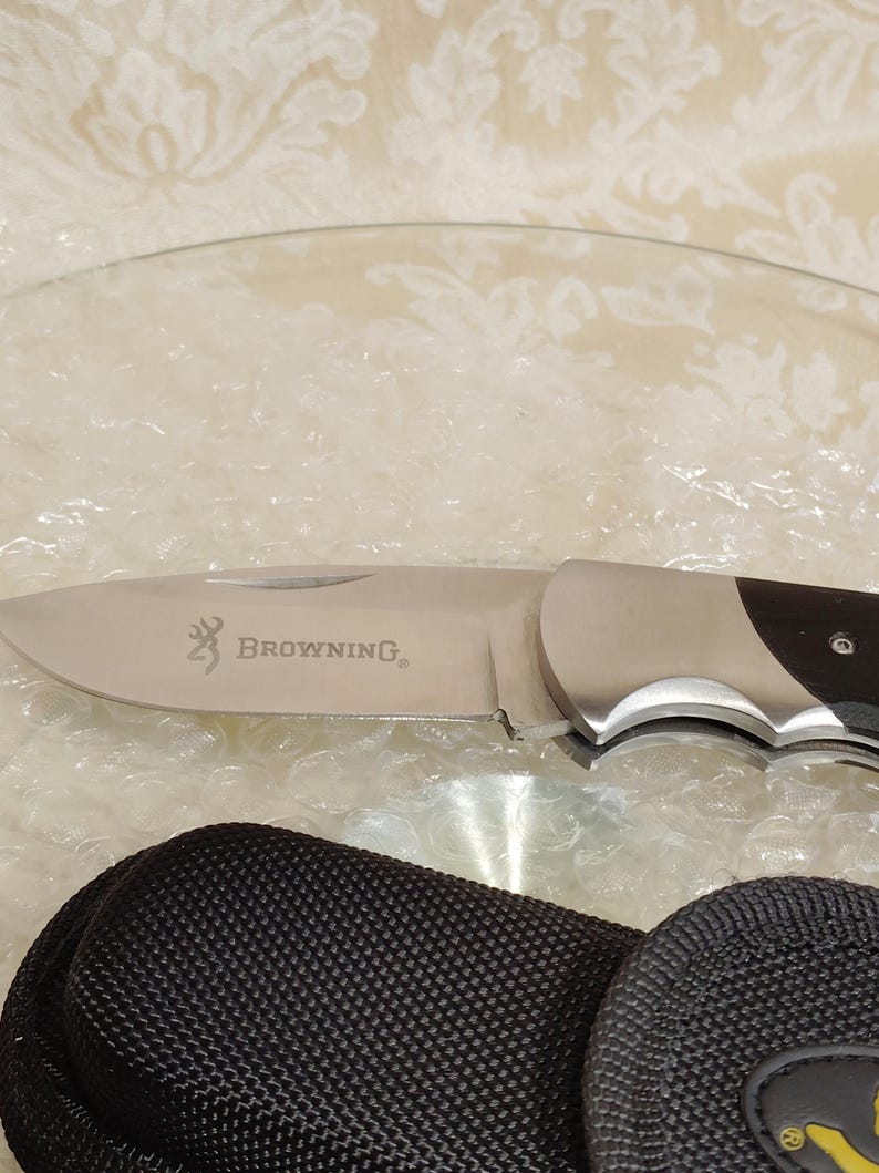 May include: A stainless steel folding knife with a dark wood handle. The blade is engraved with the Browning logo. A black nylon carrying case is included.