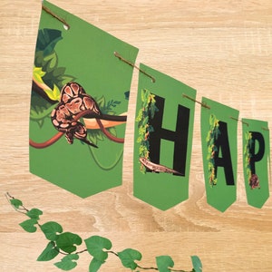 Op de afbeelding: Groene en zwarte jungle-banner met het woord "HAPPY" in zwarte letters. Elke letter staat op een aparte vlag met een groene achtergrond en afbeeldingen van slangen en hagedissen.