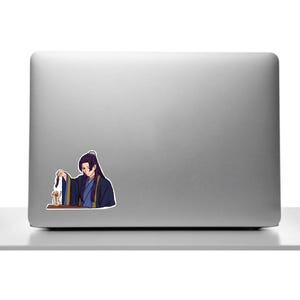 K&ouml;nnte beinhalten: Ein Aufkleber mit einer Anime-Figur in traditioneller Kleidung. Die Figur mit langen schwarzen Haaren h&auml;lt einen kleinen Gegenstand. Der Aufkleber ist auf einem silbernen Laptop angebracht.