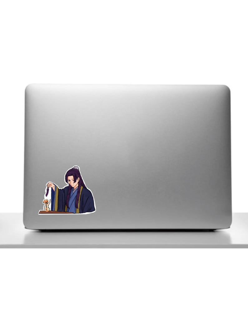 K&ouml;nnte beinhalten: Ein Aufkleber mit einer Anime-Figur in traditioneller Kleidung. Die Figur mit langen schwarzen Haaren h&auml;lt einen kleinen Gegenstand. Der Aufkleber ist auf einem silbernen Laptop angebracht.