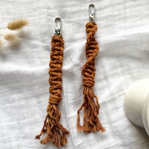 May include: Two brown macrame keychains with silver clasps. The keychains are made with a thick, twisted cord and have long tassels.
