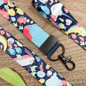 May include: Navy blue lanyards with a colorful sea life pattern. The lanyards feature various marine creatures like fish, jellyfish, and stingrays. Each lanyard has a black metal clasp and a dark blue fabric piece.