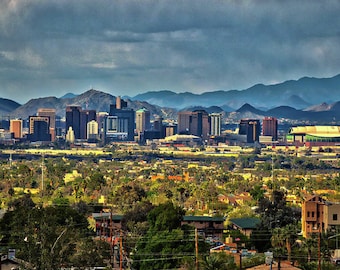 May include: A panoramic view of a city skyline with a large stadium in the foreground. The city is surrounded by mountains in the background. The sky is cloudy and overcast.