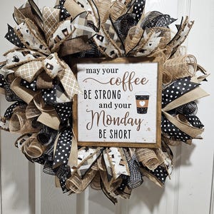 May include: A brown and black wreath with a sign that reads "May your coffee be strong and your Monday be short". The sign has a brown background with white polka dots and a coffee cup graphic.