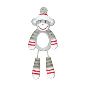 May include: A gray sock monkey baby rattle with red and white striped accents. The monkey has a smiling face, a white hat with a red pom-pom, and gray legs. The rattle is designed with a circular center.