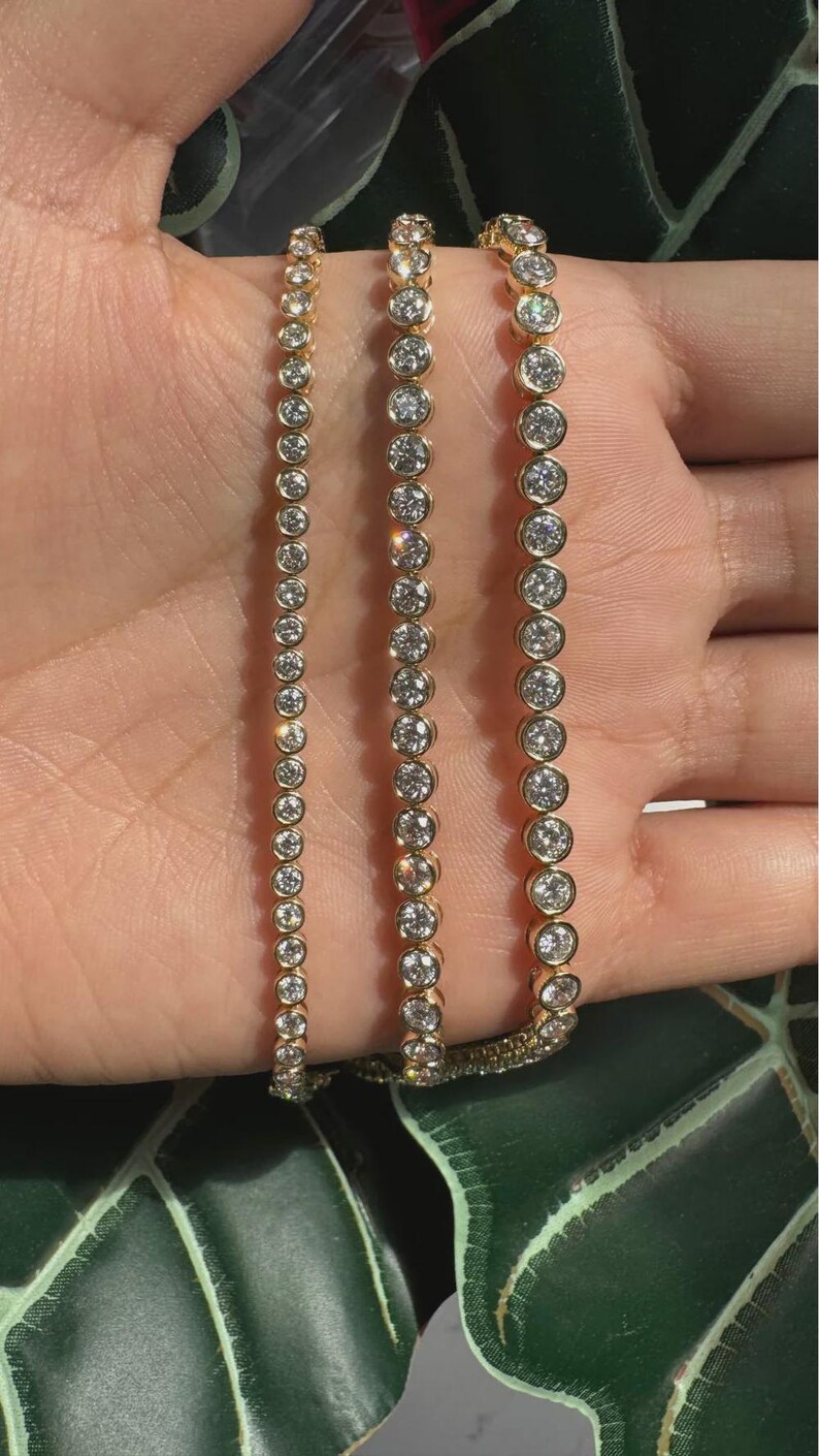 May include: Three gold-toned tennis bracelets featuring a continuous row of round, clear, bezel-set stones. Each bracelet displays a uniform design with metallic gold settings surrounding the circular, faceted, reflective white stones.