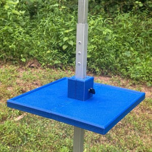 May include: A bright blue square platform tray mounted on a vertical silver metal pole. The tray features a central square housing with a black tightening knob on the side, designed to secure the platform to the adjustable telescopic metal stand.
