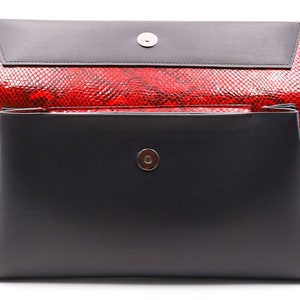 May include: A black and red clutch bag with a magnetic closure. The bag has a red snakeskin pattern and a black flap. The rectangular bag has a silver-coloured magnetic snap.