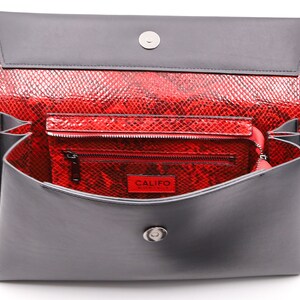 May include: A red snakeskin-effect clutch bag with a grey flap and interior. The bag contains a smaller matching wallet. The word "CALIFO" is visible on a red tag inside the wallet.