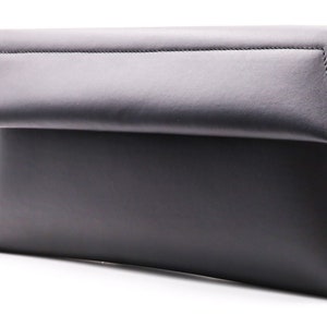 May include: A black leather clutch bag with a fold-over flap. The interior lining has a red snakeskin pattern. The bag is rectangular and has a minimalist design, suitable for various occasions.