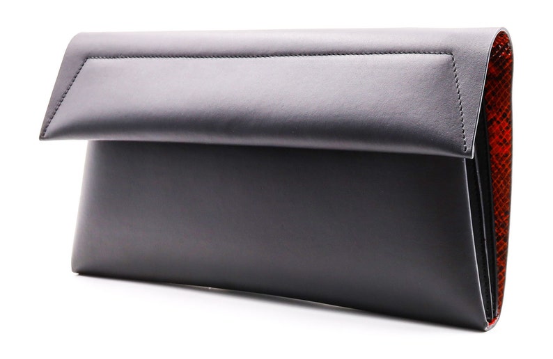 May include: A black leather clutch bag with a fold-over flap. The interior lining has a red snakeskin pattern. The bag is rectangular and has a minimalist design, suitable for various occasions.