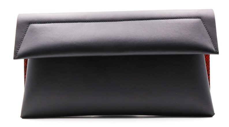 May include: A black leather clutch bag with a folded flap. The bag has a rectangular shape and a red patterned interior. The edges are neatly stitched, and the design is minimalist and modern.