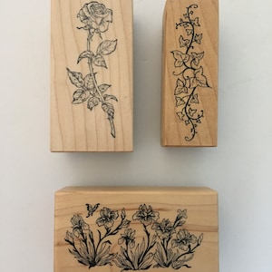 May include: Three wooden stamps with floral designs. The first stamp features a single rose with leaves and thorns. The second stamp features a vertical design of ivy vines. The third stamp features a horizontal design of irises and a butterfly.