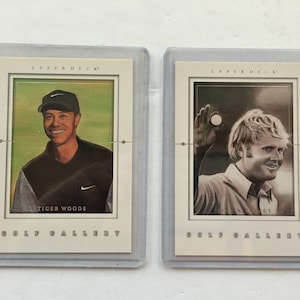 Puede incluir: Dos cromos Upper Deck Golf Gallery en fundas protectoras. Una tarjeta presenta a Tiger Woods, la otra una imagen en blanco y negro de Jack Nicklaus. Ambas tarjetas tienen un borde color crema y las palabras "GOLF GALLERY".