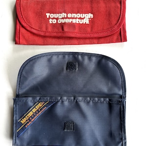 Puede incluir: Dos bolsas de tela. La bolsa superior es roja con el texto "Tough enough to overstuff" en blanco. La bolsa inferior es azul marino con cierre de velcro y una etiqueta que dice "Master Blend Coffee. It Only Tastes Expensive."