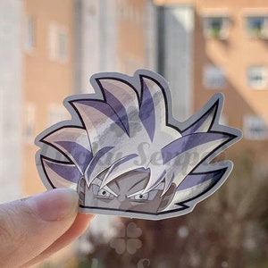 Op de afbeelding: Een sticker met een close-up van een anime-personage met wit haar en een serieuze uitdrukking. De ogen van het personage zijn wijd open en zijn wenkbrauwen zijn gefronst. De sticker is gedrukt op helder vinyl en heeft een glanzende afwerking.