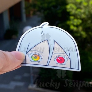 Peut inclure: Un autocollant blanc avec le visage d'un personnage de dessin animé. Le personnage a les cheveux bleus et un œil jaune et un œil rouge. L'autocollant porte le texte "Lucky Senpai" en bas.