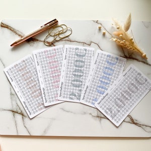 May include: Four white cards with a grid of circles, each with a number inside. The cards are labeled "Sparchallenge" and "Spare 2,000&euro;". The circles are filled with different shades of pink, blue, and gray.