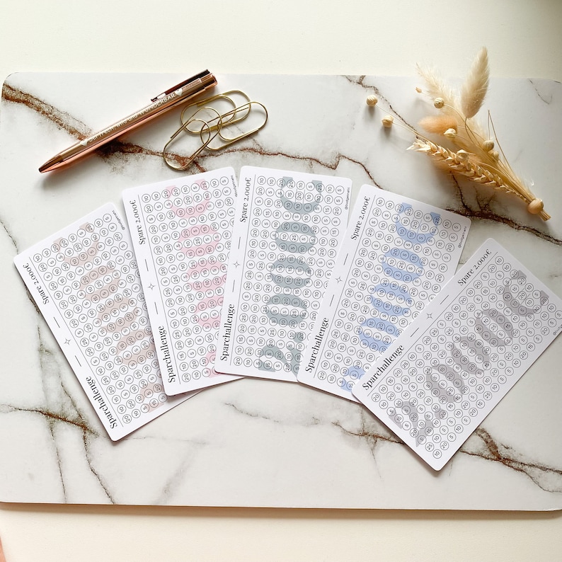 May include: Four white cards with a grid of circles, each with a number inside. The cards are labeled "Sparchallenge" and "Spare 2,000&euro;". The circles are filled with different shades of pink, blue, and gray.