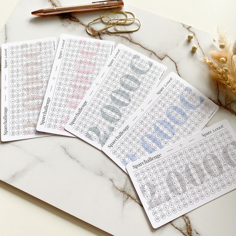 May include: Five printable cards with a light gray background and black text. Each card has a grid of circles with different colored stripes. The text on the cards reads "Sparchallenge" and "Spare 2,000&euro;".