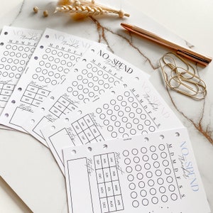 Könnte beinhalten: Vier weiße, druckbare No-Spend-Tracker-Blätter mit einem schwarz-weißen Design. Jedes Blatt hat ein Kalenderrraster mit den Monaten des Jahres und einen Bereich für Notizen. Der Text "NO-SPEND Tracker" befindet sich oben auf jedem Blatt.