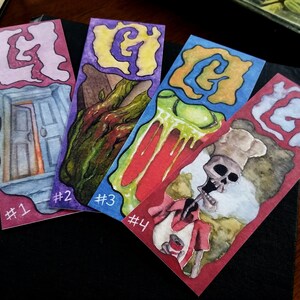 Pu&ograve; includere: Quattro segnalibri ad acquerello con un tema spettrale. Ogni segnalibro presenta un'illustrazione diversa con una lettera "G" al centro. I segnalibri sono numerati da 1 a 4.
