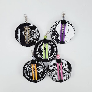 May include: Five black round zippered pouches with different graphic designs and text. The pouches have silver metal rings and black and white text. The text on the pouches includes "Disclose", "D-Beat", "Raw Punk", "Human Lie Liberation", and "Liberation Ration".