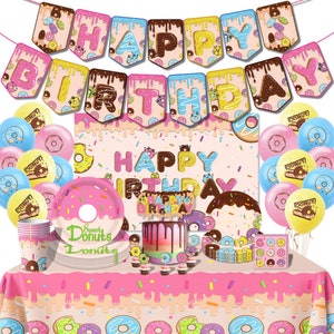 Op de afbeelding: Donut-thema verjaardagsfeest benodigdheden, waaronder een roze tafelkleed, een banner met de tekst "Happy Birthday", borden, bekers en ballonnen.