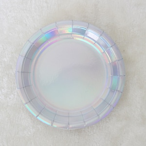 May include: A white iridescent paper plate with a scalloped edge. The plate is made of paper and has a shiny, iridescent finish.