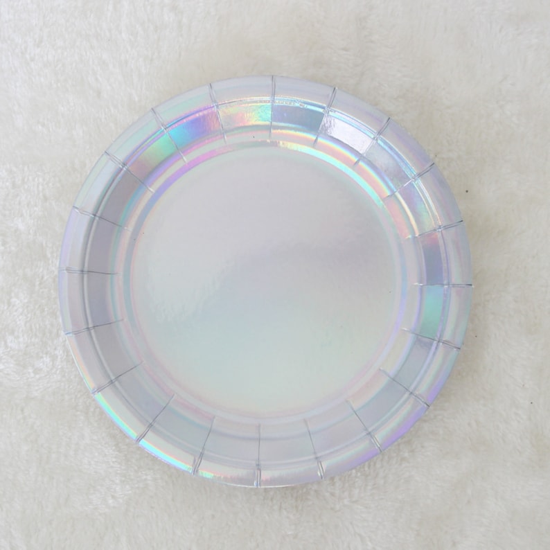 May include: A white iridescent paper plate with a scalloped edge. The plate is made of paper and has a shiny, iridescent finish.