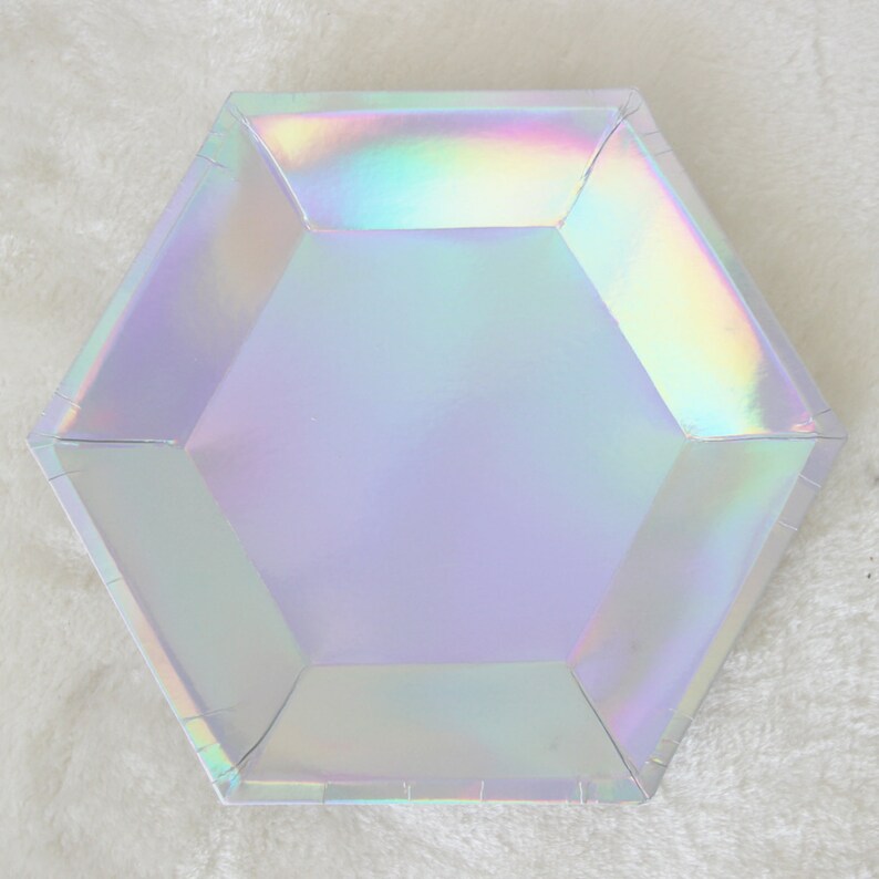 May include: A hexagonal iridescent paper plate with a light purple interior. The plate is made of paper and has a shiny, holographic finish.
