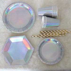 May include: A set of iridescent silver party supplies, including round and hexagonal plates, cups, and striped straws.