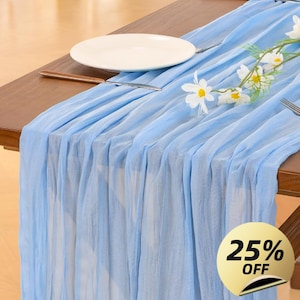 Peut inclure: Chemin de table en mousseline bleu clair sur une table en bois, avec une assiette blanche, des couverts et des décorations florales. Un autocollant doré avec "25% OFF" est dans le coin inférieur droit.