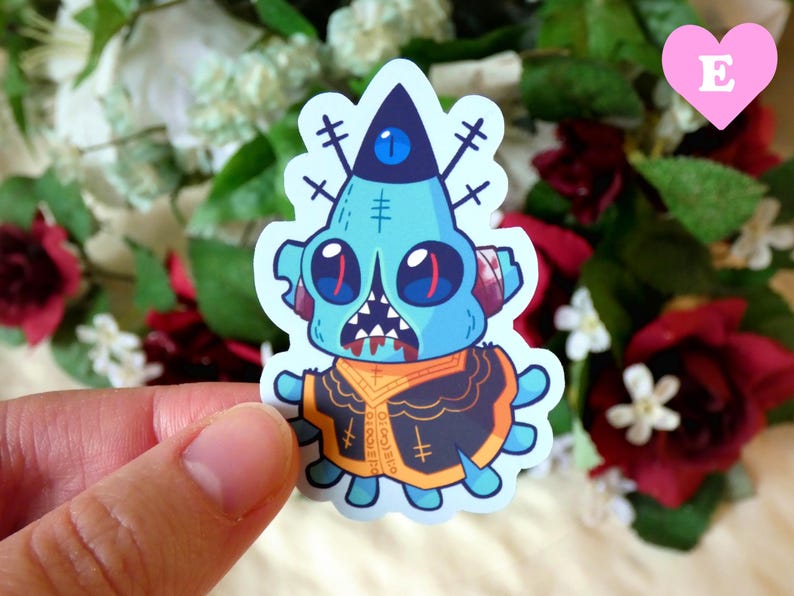 May include: A blue and orange cartoon monster sticker with a single eye and stitches on its face. The monster is wearing a black and orange jacket with a cross pattern.