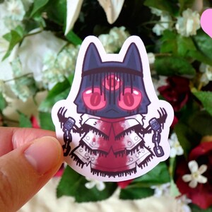 May include: A sticker featuring a cartoon character with a black and red mask, a white robe, and chains. The character has three red eyes and is holding a chain in each hand.