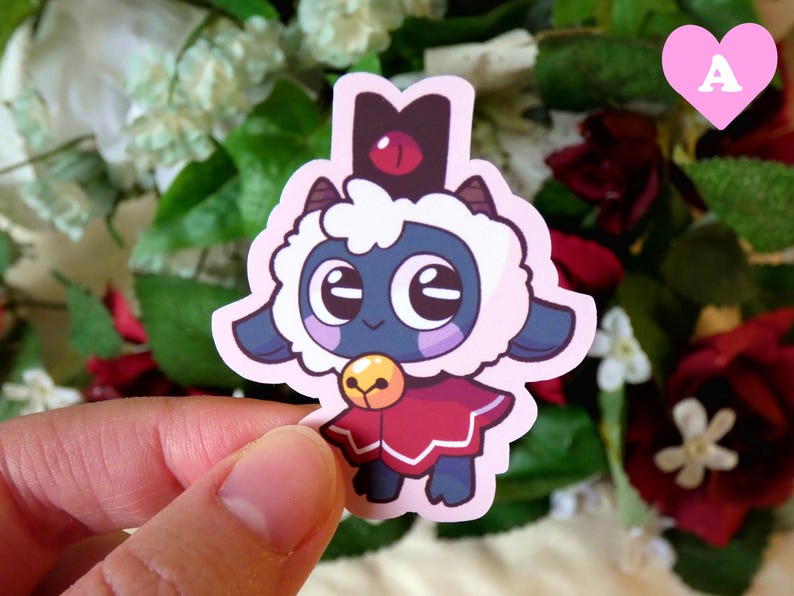 May include: A sticker of a cartoon sheep wearing a red and white cape and a black crown with a red eye. The sheep has a blue face and large, white eyes.