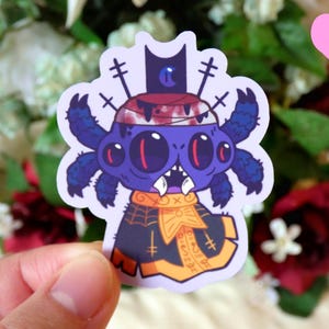 May include: A purple and blue spider wearing a black and gold hat and a black and gold cape. The spider has three eyes and a toothy grin. The sticker is on a white background.