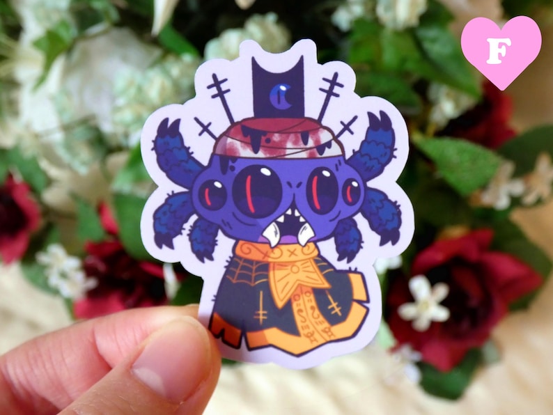 May include: A purple and blue spider wearing a black and gold hat and a black and gold cape. The spider has three eyes and a toothy grin. The sticker is on a white background.