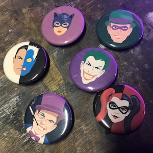 May include: Six circular pinback buttons featuring illustrated portraits of comic book characters. The designs include Catwoman, The Riddler, Two-Face, The Joker, The Penguin, and Harley Quinn, each rendered in a distinct color palette and style.