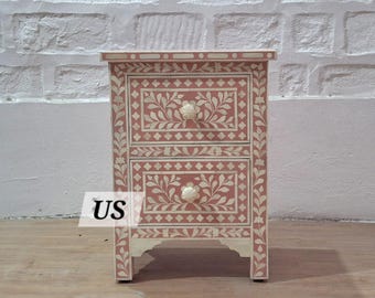 May include: A two-drawer nightstand with a pink base and white bone inlay floral design. The drawers have bone inlay knobs.