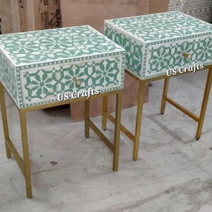 May include: Two matching green and white bone inlay nightstands with gold metal frames. Each nightstand has one drawer with a bone inlay front and a gold knob. The nightstands are labeled "US Crafts".